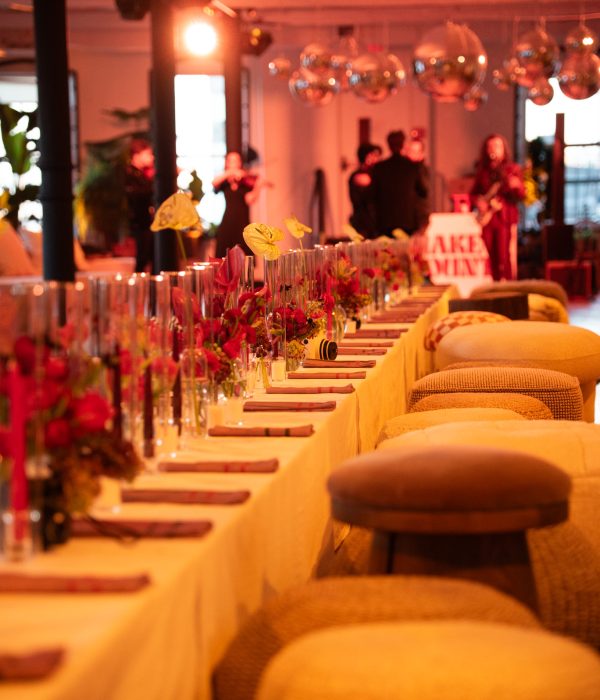 A long dinner table adorned with flowers and candles, with vibrant lighting in the background.