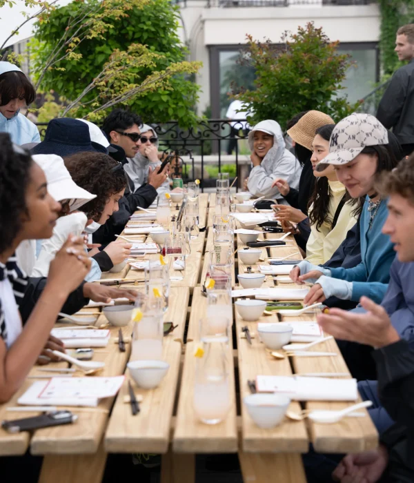 A group of people seated at a long wooden table, enjoying a meal outdoors on a cloudy day.